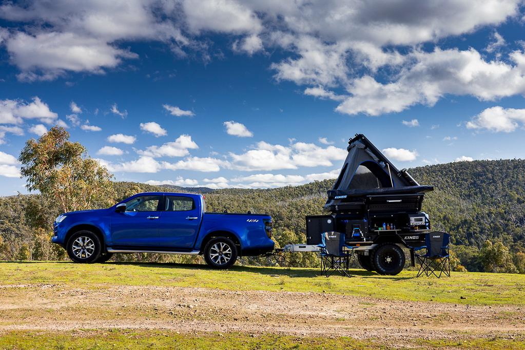 Off-road 4x4 truck with a camper trailer and rooftop tent in the mountains.